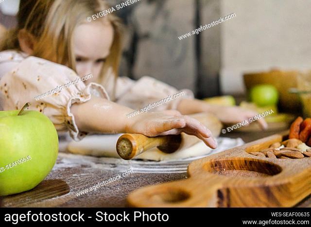 Girl using rolling pin in kitchen at home