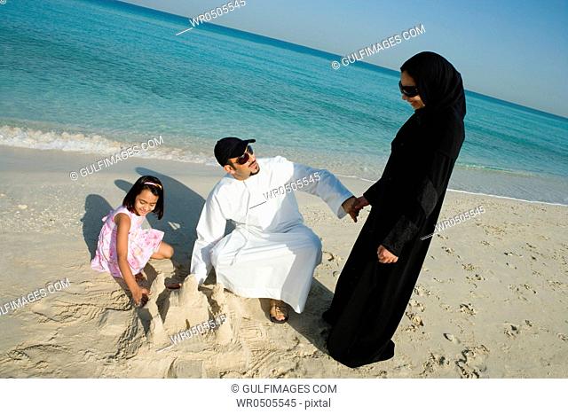 Girl playing with parents in sand, elevated view