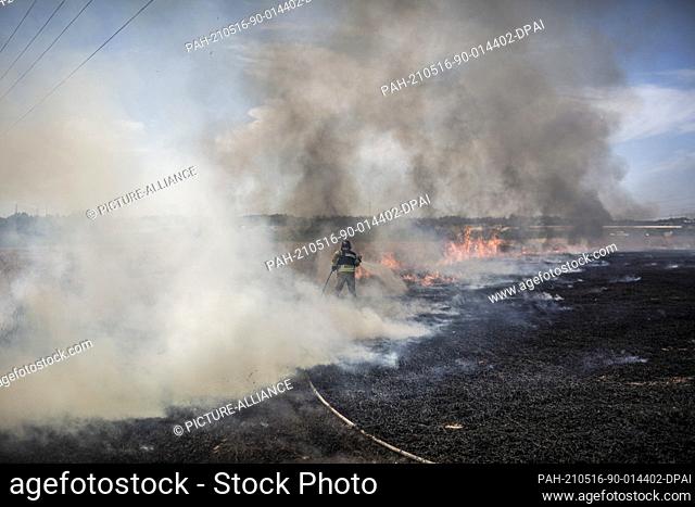 16 May 2021, Israel, Ashkelon: An Israeli firefighter battles a blaze in a field caused by a rocket fired from Gaza Strip towards Israel