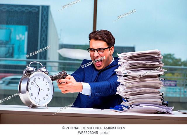 Businessman with pile stack of paper paperwork and an alarm clock working in the office
