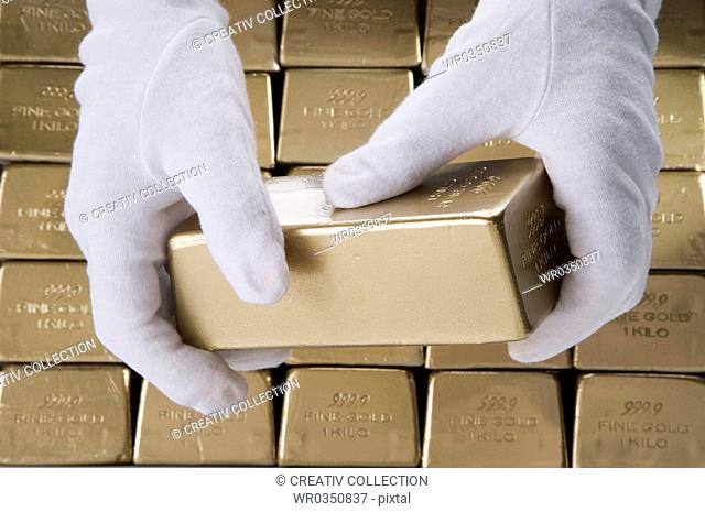 person wearing white gloves lifting up a gold bar