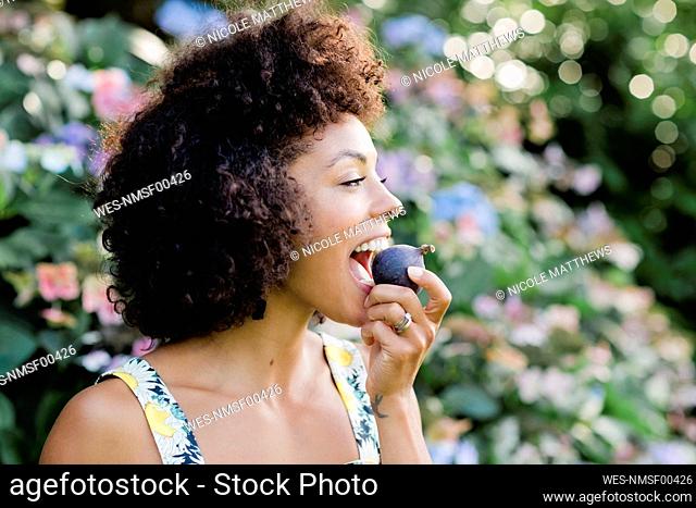 MId adult woman eating figwhile standing in front of flowering plant at park