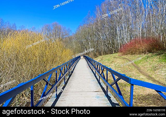 Wooden pedestrian bridge over the marshy ravine. Nice sunny day in April