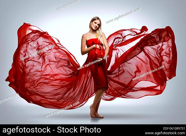 Beautiful young pregnant woman in red dress on grey background. Copy space
