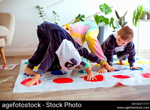 The children dressed in animal kigurumi sitting on the floor in the room. The kids in pajamas play twister