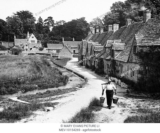 A water carrier on Arlington Row, Bibury, Gloucestershire, England. These cottages, fine examples of Cotswold architecture