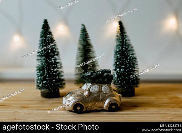 Still life, small golden car with a fir tree on the roof in front of fir trees and a chain of lights, romantic Christmas mood