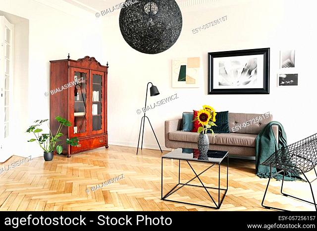 Yellow sunflowers on a black, marble coffee table and framed art on a tall white wall in an elegant living room interior