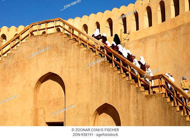 Schulkinder auf Exkursion ersteigen die Treppe zum Wehrgang der Burg von Nizwa, Nizwa, Sultanat Oman / School kids on an excursion climbing the stairs to the...