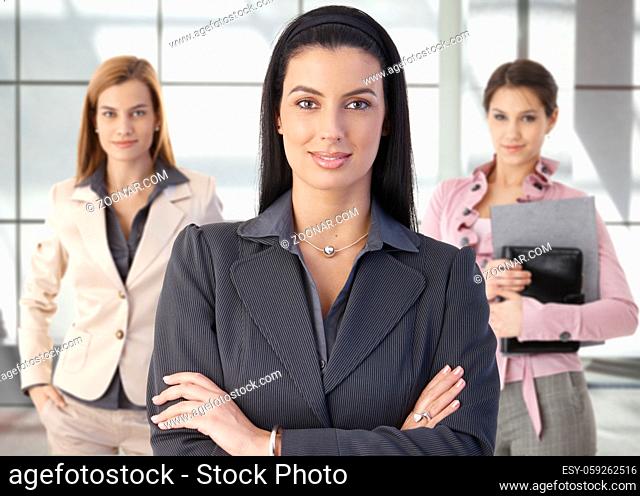 Team portrait of happy businesswomen standing on office corridor, looking at camera, smiling