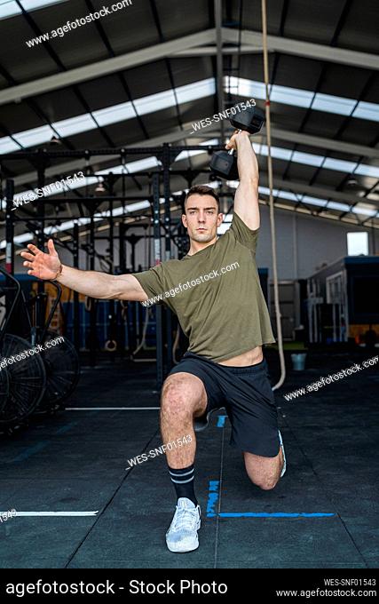 Focused male athlete exercising while holding dumbbell in gym