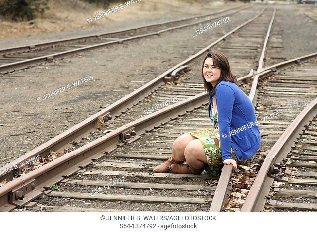 A happy young woman sitting on train tracks outdoors