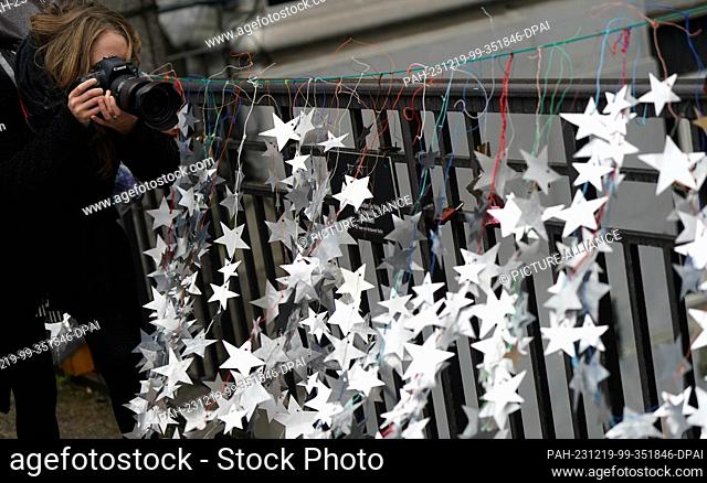 19 December 2023, Hamburg: A woman photographs the homemade stars made from aluminum lids from yogurt and pudding cups on the Michaelis Bridge in the city...