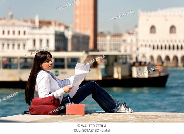Young woman reading map on waterfront opposite St Marks Square, Venice, Italy