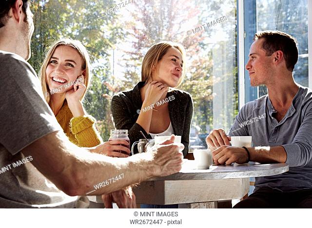 Four people sitting at a table talking, with mugs and jars of smoothies