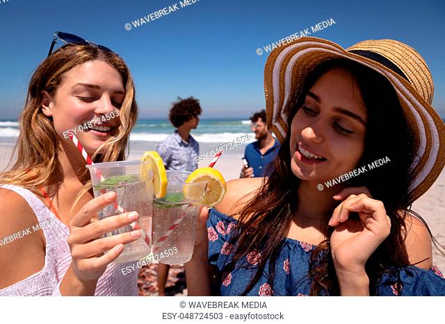 Beautiful young woman toasting cocktail glasses at beach in the sunshine