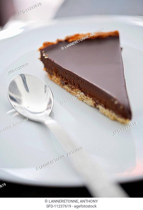 A slice of chocolate tart on a plate with a spoon