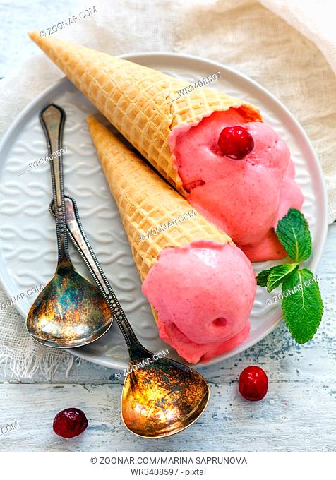 Cranberry ice cream in waffle cones on a white plate and dessert spoons, selective focus