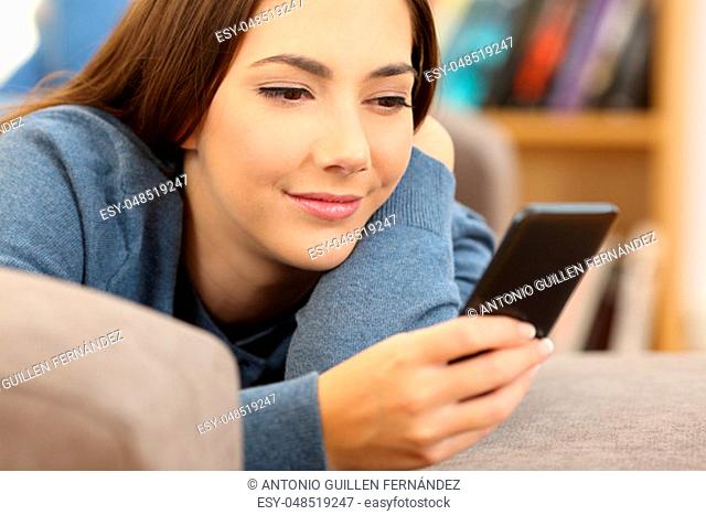 Girl reading mobile phone content lying on a sofa in the living room at home