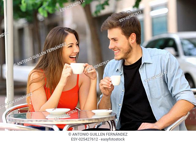 Happy couple or friends flirting talking and drinking in a restaurant terrace