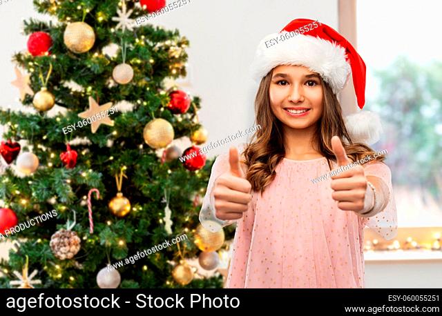 happy teenage girl in santa hat showing thumbs up