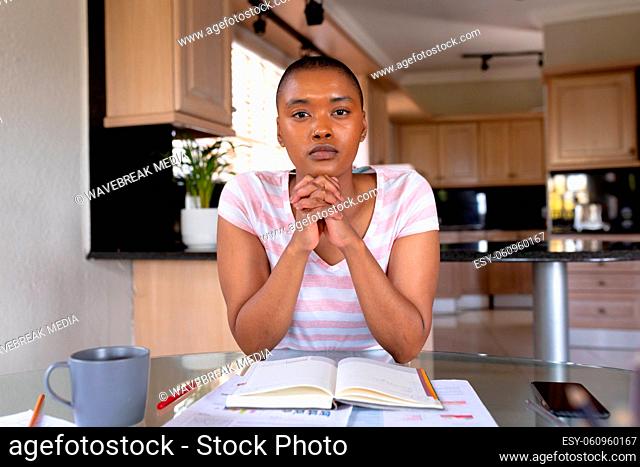 Portrait of biracial female freelancer sitting with hands clasped at home office