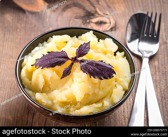 Mashed potatoes with fresh red basil in dark bowl on wooden background. Copy space