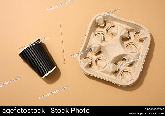 brown disposable corrugated cardboard cup, wooden stirring stick and holder on brown background. View from above
