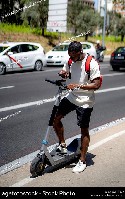 Young man with electric push scooter using smart phone on road