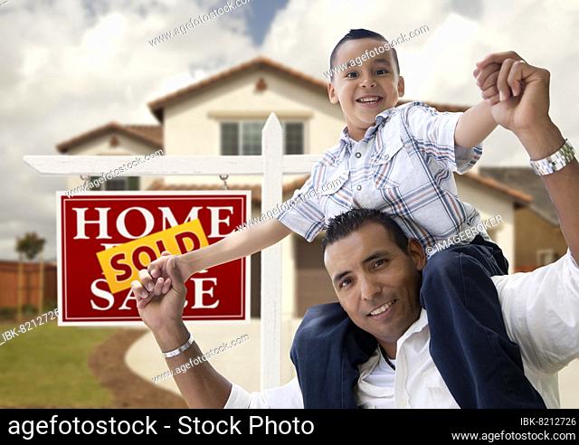 Happy hispanic father and son in front of new house and sold real estate sign