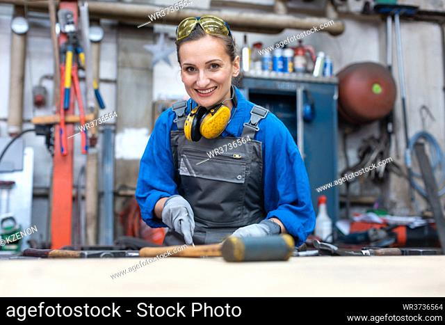Woman worker marking workpiece in her workshop looking into camera
