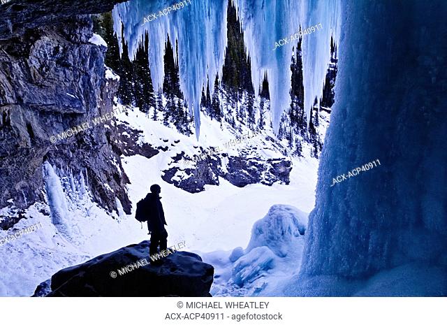 Hiker dwarfed by giant icicles, behind Panther Falls in Winter, Banff National Park, Alberta, Canada