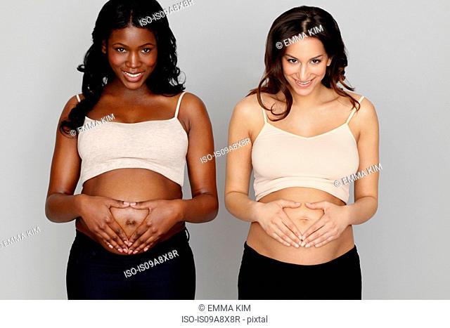 Two pregnant women making heart shapes with hands on stomachs