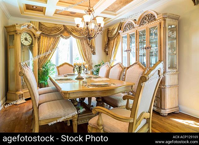 Antique style wooden dining table with upholstered high back chairs, buffet and grandfather clock in dining room inside a luxurious residential home, Quebec
