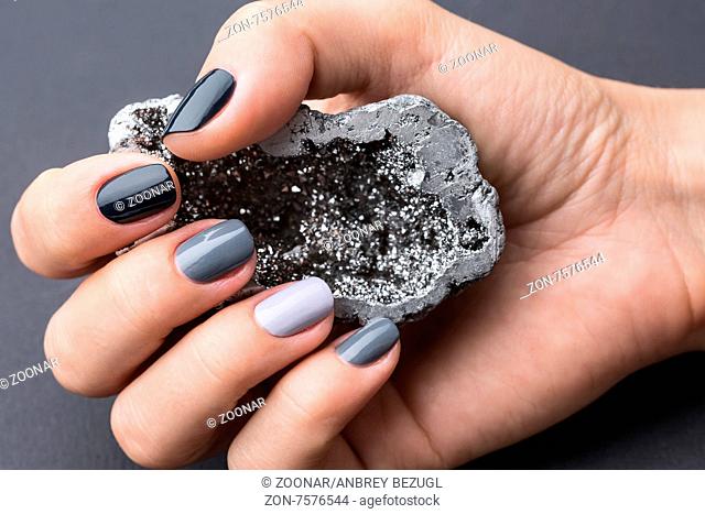 Well-groomed female hand with a stylish manicure holding a beautiful textured silver mineral. Nail painted gray paint different tonality