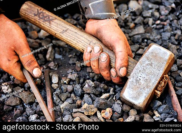 Detail of dirty hands holding hammer and rod - blacksmith