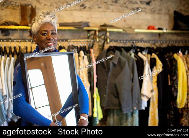 Portrait confident senior female shop owner with mirror in boutique