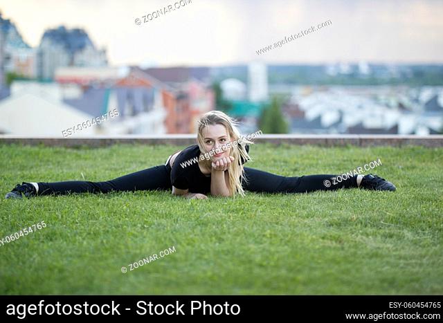 Smiling young girl on the green grass performs twine, on background cityscape, horizontal