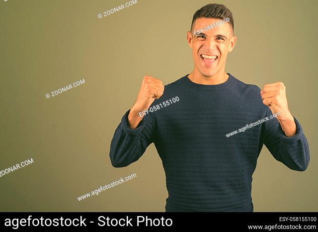 Studio shot of young handsome man wearing sweater against colored background