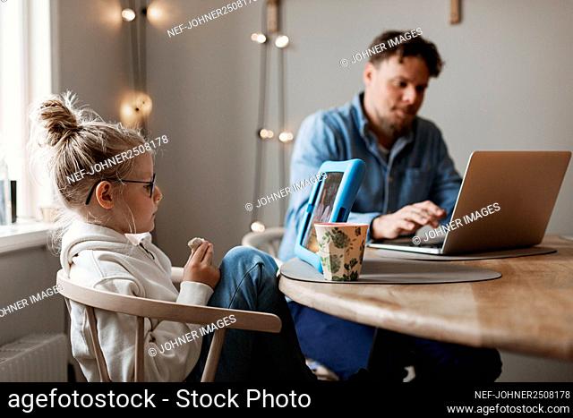 Girl using digital tablet, father in background