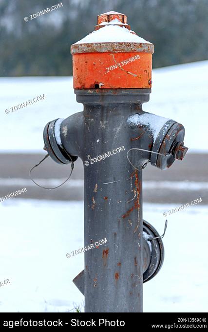 Oberer Teil eines alten rostigen Oberflur-Hydranten an einer Nebenstraße in Bayern im verschneiten Winter. Upper part of an old rusty overhead hydrant on a side...