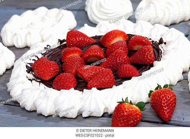 Meringues and meringue baked pastry case with chocolate icing garnished with strawberries on grey wood