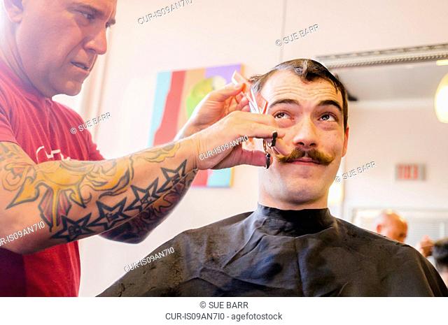 Young man with handlebar moustache having his hair cut