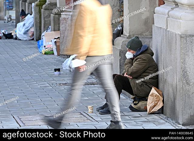 Public life in times of the coronavirus pandemic on February 19th, 2021 in Munich. A beggar, homeless person, bum sits with a face mask