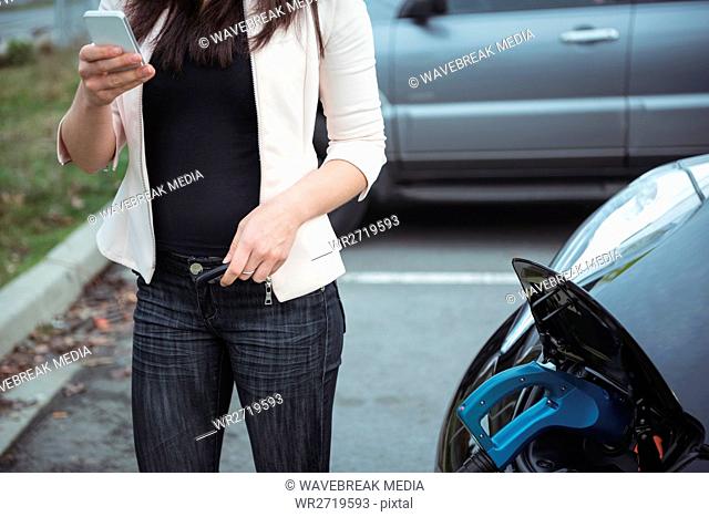 Mid section of woman using mobile phone while charging electric car