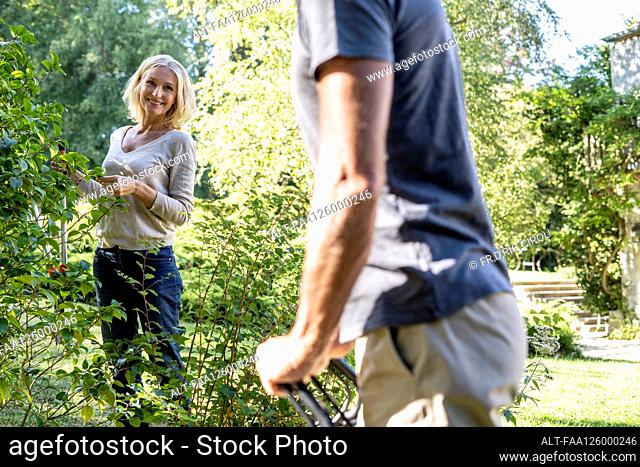 Smiling mature woman with secateurs looking at her husband in backyard