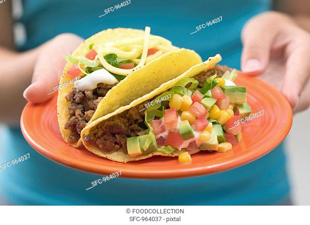 Woman holding two tacos on a plate