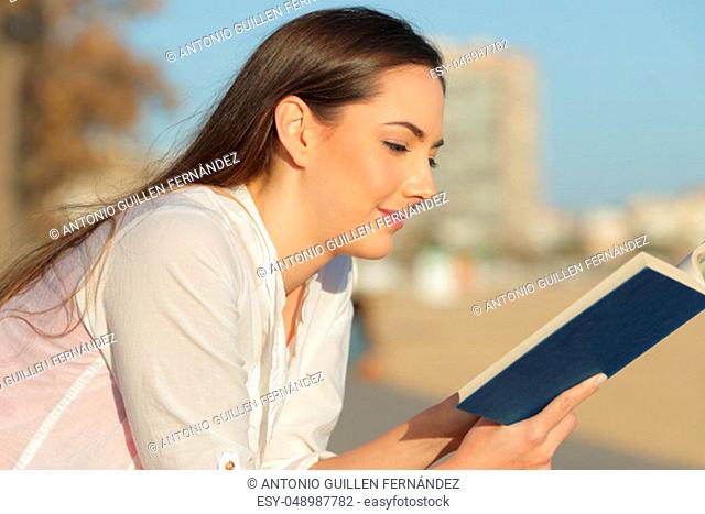 Relaxed woman reading a paper book a sunny day sitting on the beach
