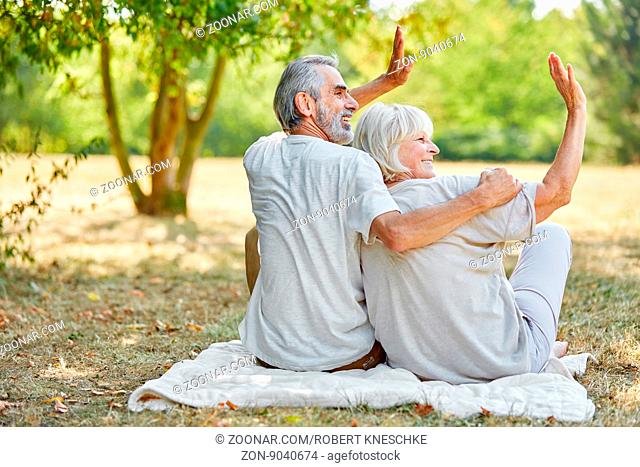 Paar Senioren sitzt entspannt im Sommer im Park und winkt fröhlich