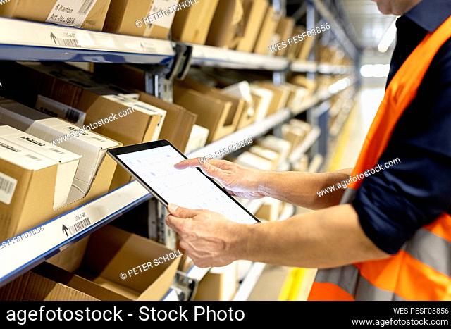 Worker checking inventory through tablet PC by rack in warehouse